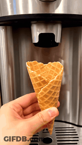 A Person Is Holding A Waffle Cone In Front Of A Coffee Machine GIF