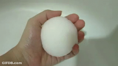 A Person Is Holding A White Ball In Their Hand Over A Sink . GIF
