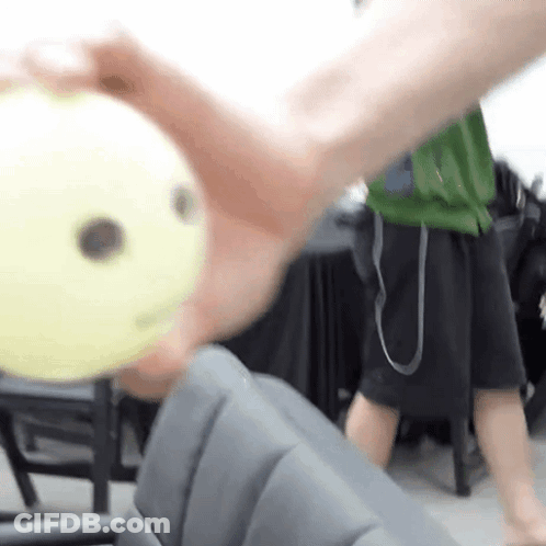 A Person Is Holding A Yellow Ball In Their Hand With A Smiley Face On It . GIF