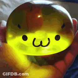 A Person Is Holding A Yellow Sphere With A Face On It . GIF