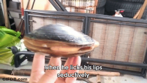 A Person Is Holding An Oyster That Says When He Licks His Lips Seductively On It GIF
