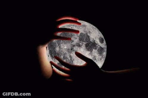 A Person Is Holding The Full Moon In Their Hands In The Dark . GIF