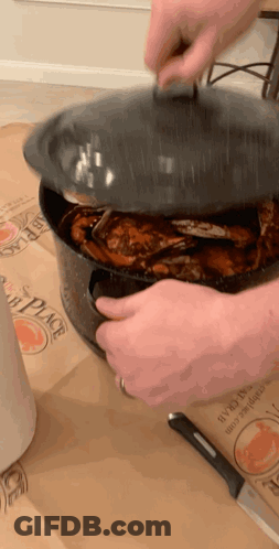 A Person Is Holding The Lid Of A Pot Of Crabs On A Table GIF