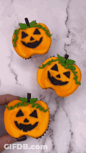A Person Is Holding Three Cupcakes Decorated To Look Like Pumpkins For Halloween GIF