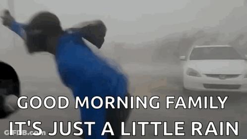 A Person Is Jumping In The Air In Front Of A Car In The Rain . GIF