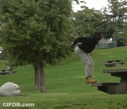 A Person Is Jumping In The Air Near A Picnic Table In A Park GIF