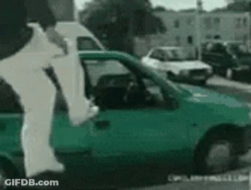 A Person Is Jumping Out Of A Green Car On A Street GIF