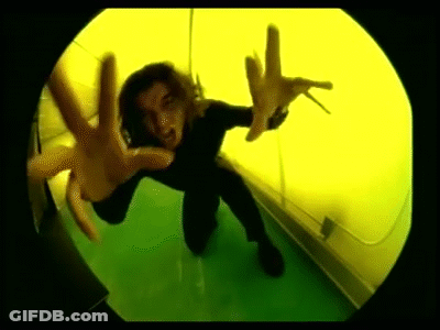 A Person Is Kneeling Down In Front Of A Yellow Wall And Making A Hand Gesture . GIF