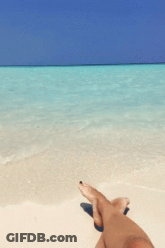 A Person Is Laying On A Beach With Their Feet Crossed GIF