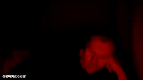 A Person Is Laying On A Bed In A Dark Room With A Red Light Coming Out Of The Corner . GIF
