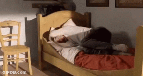 A Person Is Laying On A Bed In A Room With A Yellow Chair . GIF