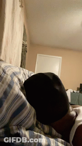 A Person Is Laying On A Bed With A Hat On Their Head GIF