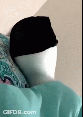 A Person Is Laying On A Bed With A Hat On Their Head GIF