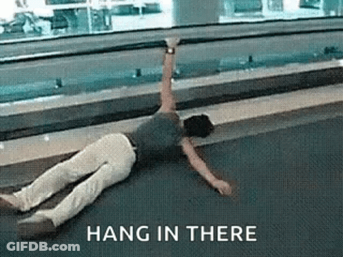 A Person Is Laying On The Floor With A Sign That Says Hang In There Above Them . GIF
