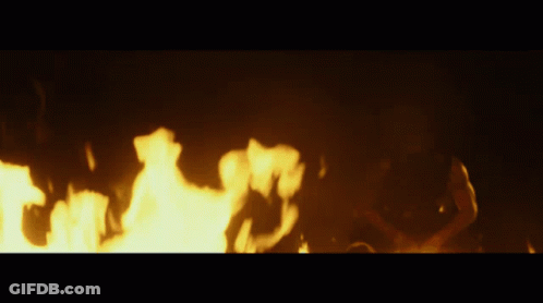 A Person Is Laying On The Ground In Front Of A Large Fire GIF