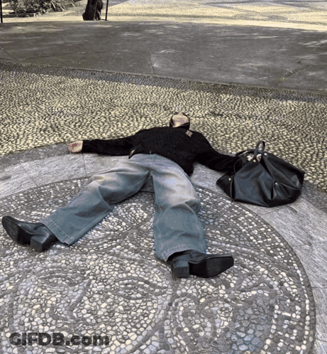 A Person Is Laying On The Ground With A Black Bag GIF