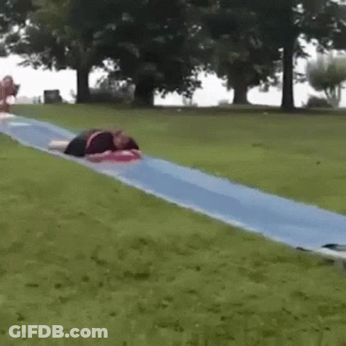 A Person Is Laying On Top Of A Blue Water Slide In A Park . GIF