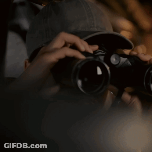A Person Is Looking Through Binoculars With A Hat On GIF