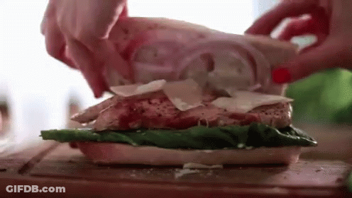 A Person Is Making A Sandwich With Chicken , Lettuce , Cheese And Onions On A Cutting Board . GIF