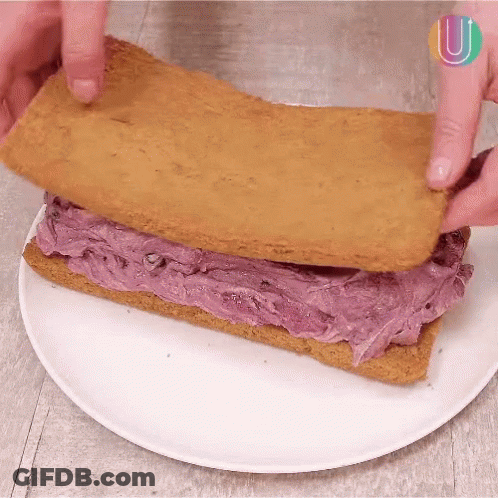 A Person Is Making A Sandwich With Purple Frosting On A White Plate .. GIF