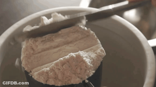 A Person Is Measuring Flour In A Measuring Cup With A Knife GIF