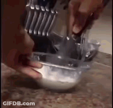 A Person Is Mixing Something In A Bowl With A Knife And Spoon . GIF