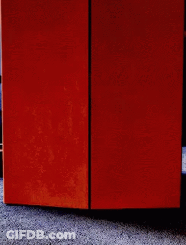 A Person Is Peeking Out From Behind An Orange Box On The Floor . GIF