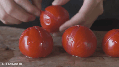 A Person Is Peeling Three Tomatoes On A Wooden Table GIF