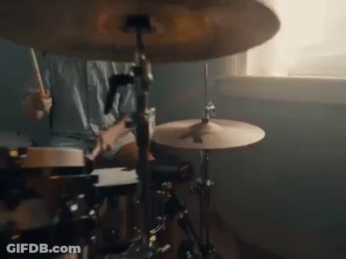 A Person Is Playing Drums In Front Of A Window In A Room . GIF