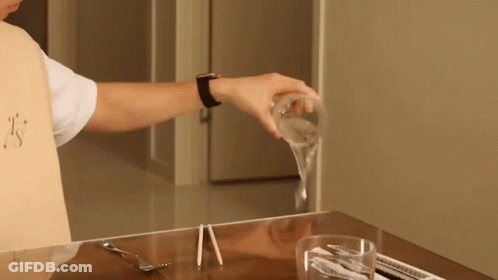 A Person Is Pouring A Glass Of Water On A Table With Chopsticks GIF