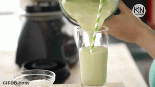 A Person Is Pouring A Green Smoothie Into A Glass With A Green Straw . GIF