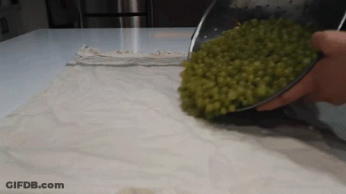 A Person Is Pouring Green Peas Into A Bowl On A Cloth GIF