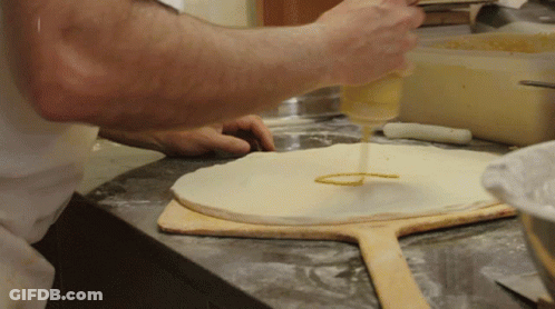 A Person Is Pouring Sauce On A Pizza Dough On A Wooden Paddle GIF
