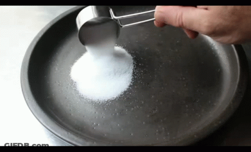 A Person Is Pouring Sugar Into A Pan With A Measuring Cup GIF