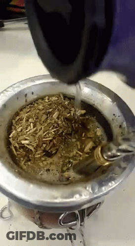 A Person Is Pouring Water Into A Metal Bowl With A Spoon In It GIF