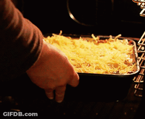 A Person Is Putting A Casserole Dish In The Oven GIF