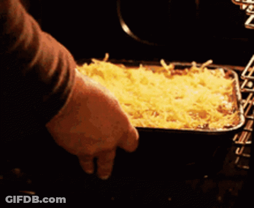A Person Is Putting A Casserole Dish In The Oven GIF