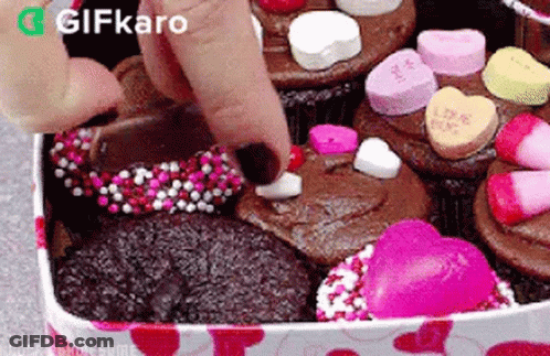 A Person Is Putting A Heart On A Cupcake In A Box Filled With Cupcakes . GIF