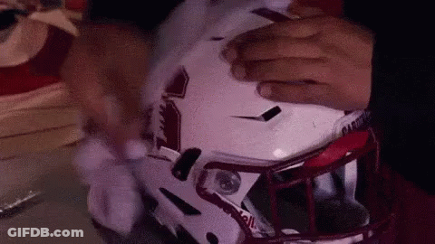A Person Is Putting On A Football Helmet With Their Hands . GIF