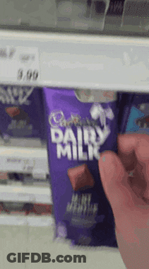 A Person Is Reaching For A Cadbury Dairy Milk Bar In A Store GIF