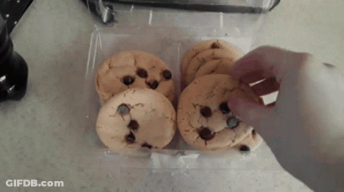 A Person Is Reaching For A Chocolate Chip Cookie From A Plastic Container GIF