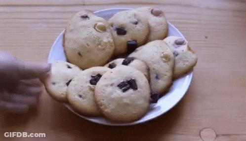 A Person Is Reaching For A Cookie On A Plate Of Cookies GIF