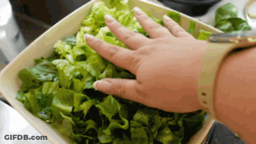 A Person Is Reaching Into A Bowl Of Lettuce With Their Hand GIF