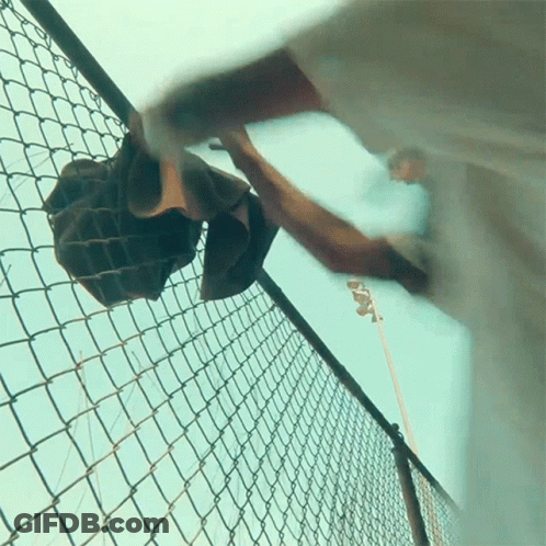 A Person Is Reaching Over A Chain Link Fence GIF
