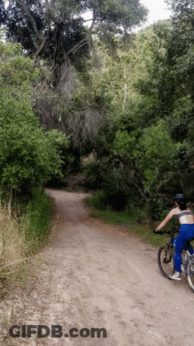 A Person Is Riding A Bike Down A Dirt Road GIF