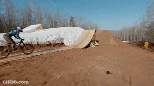 A Person Is Riding A Bike On A Dirt Track With A Red Bull Sign In The Background GIF