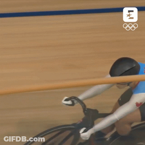 A Person Is Riding A Bike On A Track With The Olympics Logo In The Background . GIF