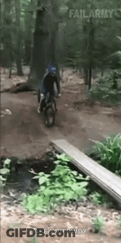 A Person Is Riding A Bike Over A Wooden Bridge In The Woods GIF