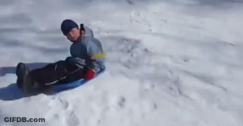 A Person Is Riding A Sled Down A Snow Covered Hill GIF