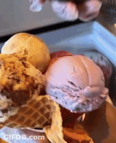 A Person Is Scooping Ice Cream Out Of A Waffle Cone In A Freezer . GIF